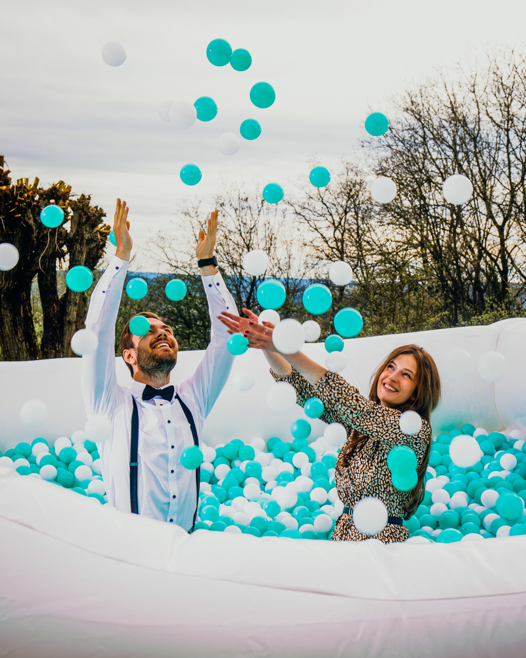 Zwei lachende Erwachsene, ein Mann und eine Frau, haben Spaß in einem Bällebad mit blau-weißen Bällen bei einem Outdoor-Event.